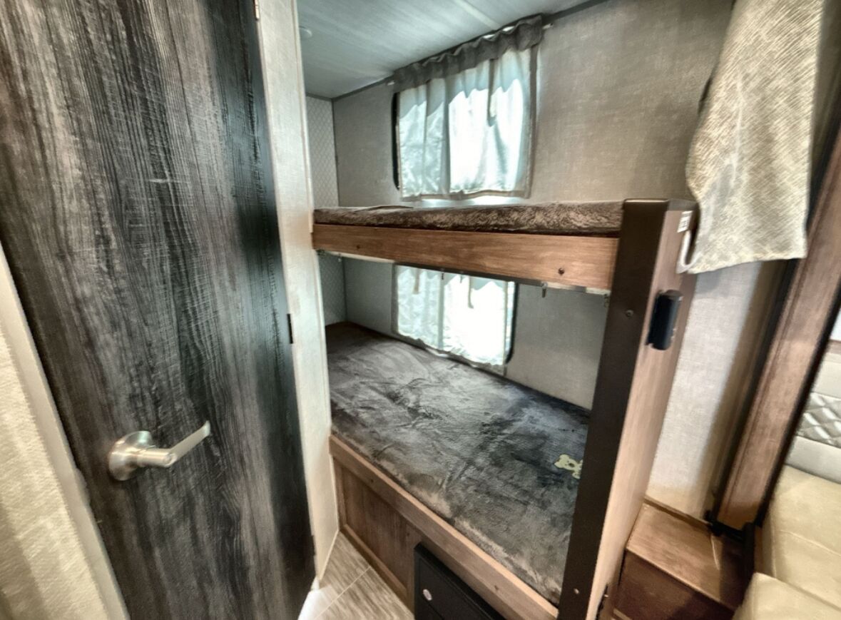 Una cama individual en un cuarto estrecho con una puerta de madera y una ventana con cortinas.
