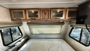 Interior compacto de una caravana con cama, televisor y armarios de madera.