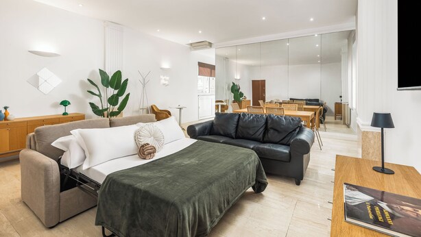 Un salon moderne avec un canapé, un lit et un coin repas à l’arrière-plan.