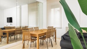 Un espace repas moderne avec une table en bois et des chaises en osier, un canapé en cuir noir et une grande plante verte.