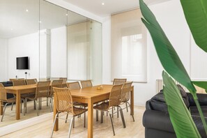 A modern dining area with a wooden table and wicker chairs, a black leather sofa, and a large green plant. - Atrhome- Penthouse Tritone (Rome)