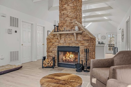 A modern living room with a stone fireplace, white walls, and a high ceiling.