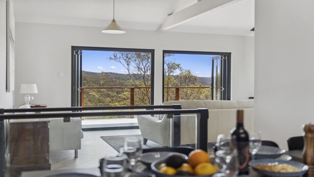 A modern dining area with a view of a mountainous landscape through large windows. - Blue Mountains Views (WENTWORTH FALLS)