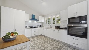 A modern kitchen with white cabinets, a blue range hood, a microwave, an oven, and a patterned floor. - Blue Mountains Views (WENTWORTH FALLS)