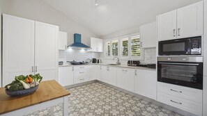 A modern kitchen with white cabinets, a blue range hood, a microwave, an oven, and a patterned floor. - Blue Mountains Views (WENTWORTH FALLS)