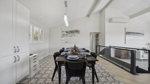 A modern dining area with a large table set for six, white cabinetry, and a view through a glass railing to a balcony. - Blue Mountains Views (WENTWORTH FALLS)