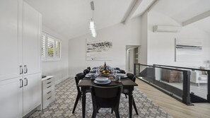 A modern dining area with a large table set for six, white cabinetry, and a view through a glass railing to a balcony. - Blue Mountains Views (WENTWORTH FALLS)
