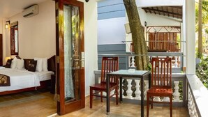 A room with a bed, a table, and chairs, a balcony with a railing, and a tree outside. - Globiquex Hotels (Duong Dong)