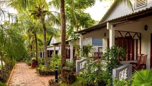 A pathway leading to a building with a covered porch, surrounded by lush greenery and palm trees. - Globiquex Hotels (Duong Dong)