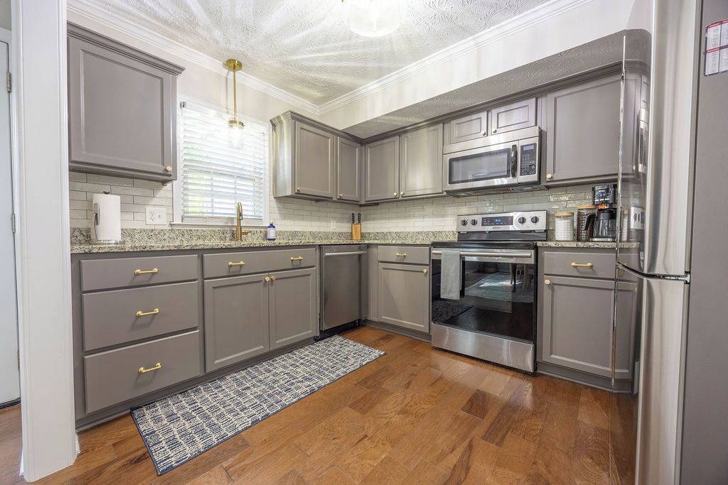 A kitchen with grey cabinets, stainless steel appliances, and a patterned rug.