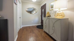 Un couloir avec un plancher en bois, une armoire grise avec une lampe, un miroir et une porte.