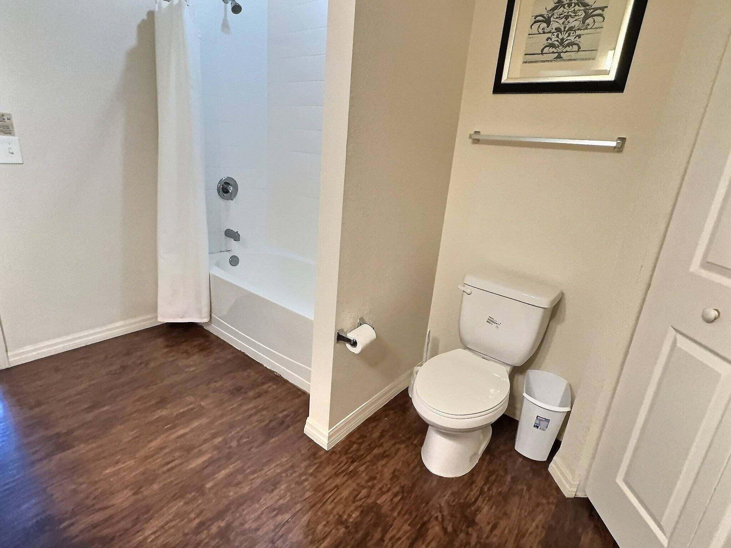 A bathroom with a bathtub, toilet, and a trash can.