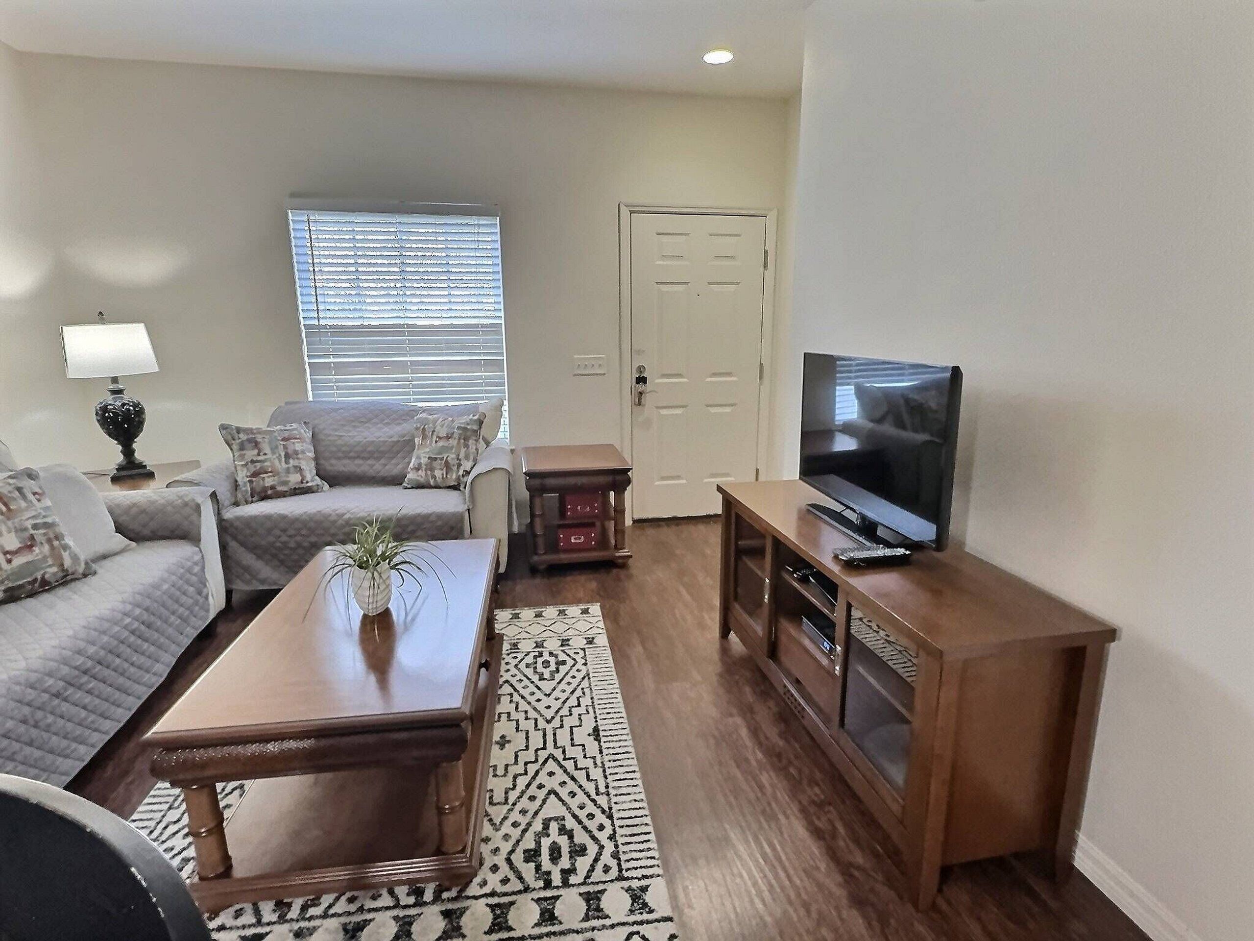 A living room with a sofa, coffee table, TV stand, and a window with blinds.