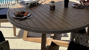 Een overdekt buitengebied met een zwembad, een tafel met stoelen en een barbecue op de achtergrond.