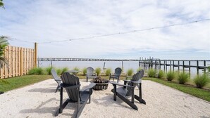 En terrass med Adirondack-stolar, en eldstad och utsikt över en brygga som sträcker sig ut över vattnet.