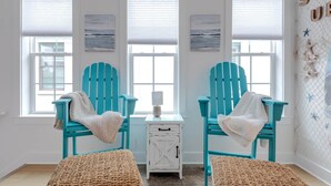 A room with two turquoise Adirondack chairs, a small white table with a lamp, and a woven rug. - Luxury 4BR/4.5BA Waterfront Home in Sandestin • Golf Carts/Golf • Pool • Beach (Miramar Beach)
