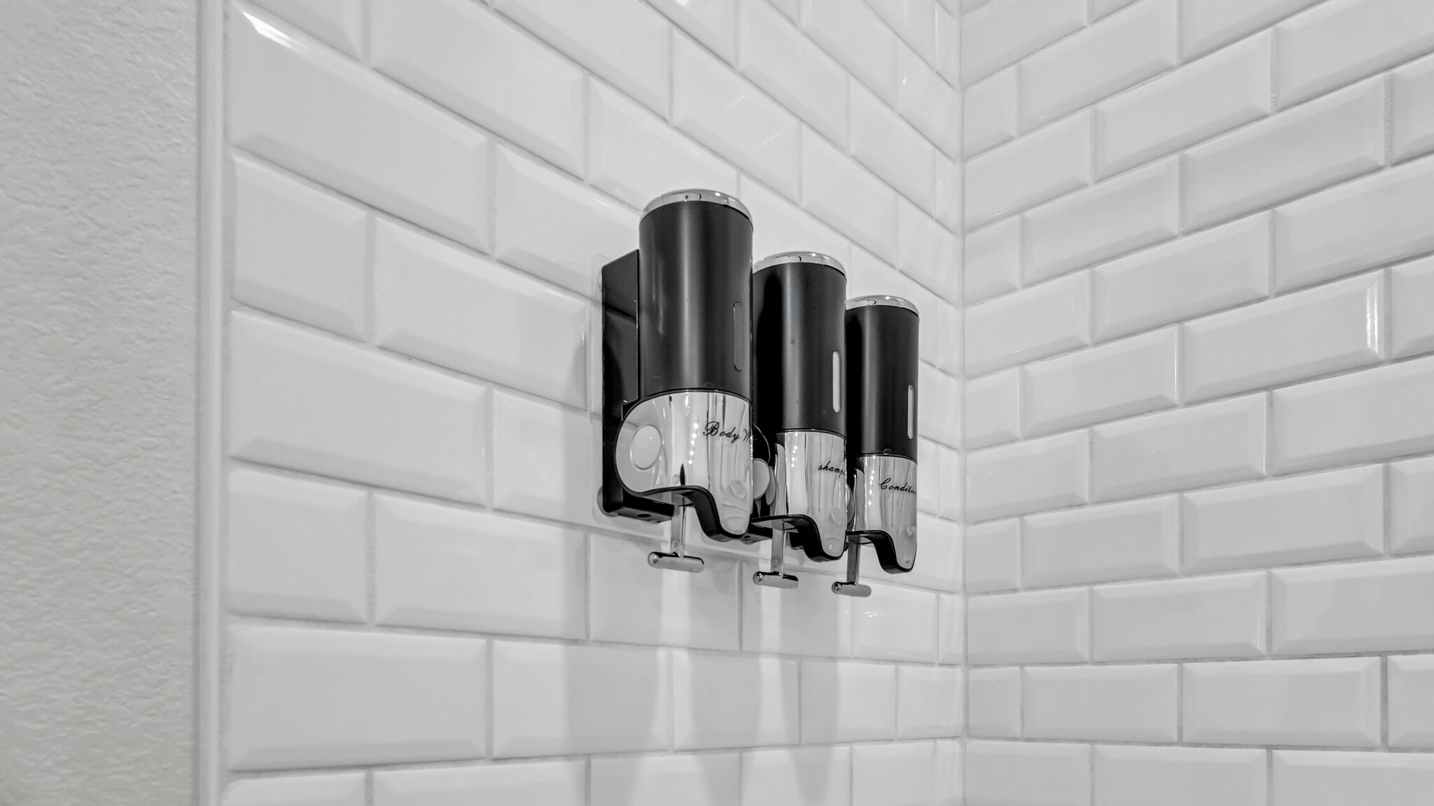 A bathroom with white subway tiles and three black soap dispensers mounted on the wall.