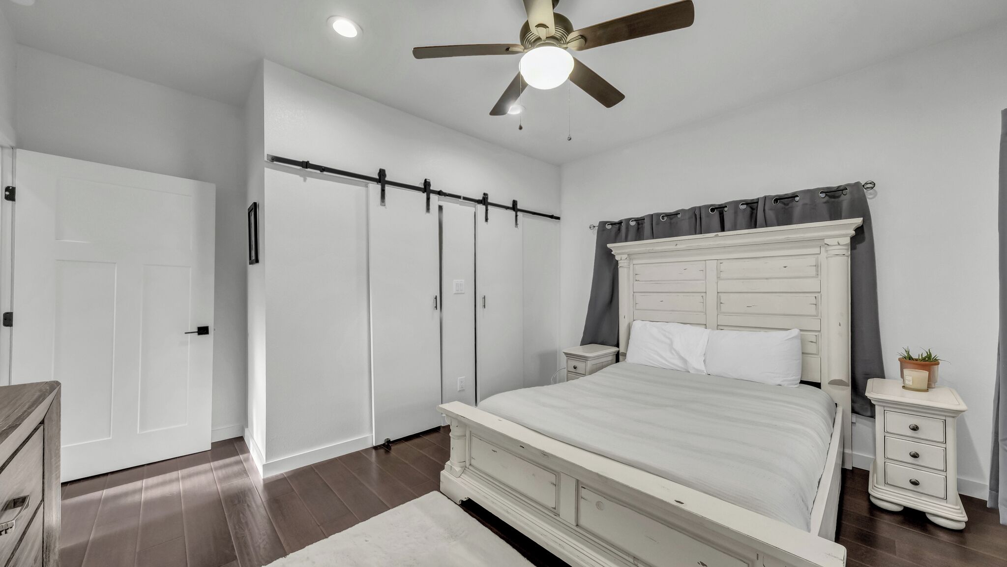 Une chambre à coucher comprenant un lit, des tables de chevet, une commode, un ventilateur de plafond et une armoire.