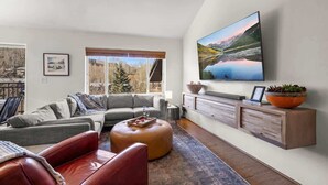 Un salon moderne avec une grande télévision, un canapé, un fauteuil en cuir rouge et un meuble en bois.
