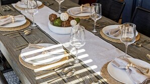Une table à manger dressée avec des assiettes, des couverts et des verres à vin, agrémentée d’un centre de table décoratif.