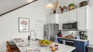 Une cuisine moderne avec des meubles blancs, un grand îlot central, des appareils en acier inoxydable et un coin repas avec des chaises marron.