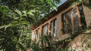 Un bâtiment rustique doté de grandes fenêtres et d’un toit en bois, entouré d’un feuillage dense.