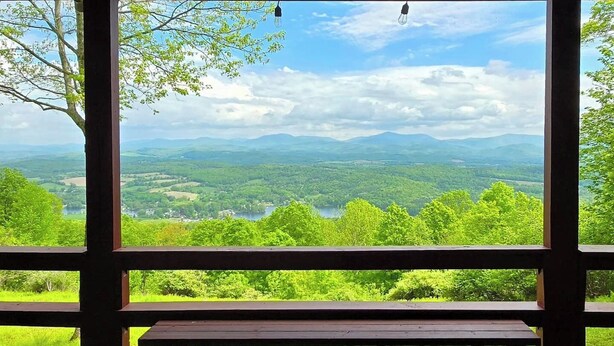 Une terrasse en bois avec un banc donnant sur un paysage magnifique, avec des montagnes et un lac.