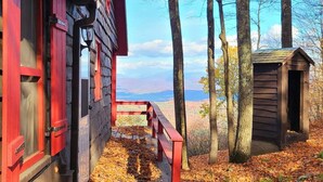 Une cabane en bois à l’extérieur rouge, dotée d’un porche et entourée d’arbres et de feuilles d’automne.