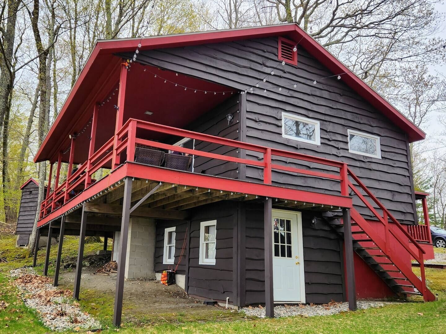 Une cabane en bois à deux étages, dotée d’un balcon rouge et d’un petit espace porche.