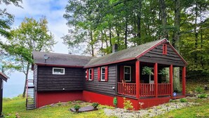 Une cabane à l’extérieur rouge, dotée d’un porche et entourée d’arbres et d’une pelouse.