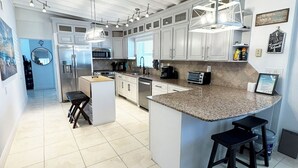 A modern kitchen with white cabinets, a granite countertop, and a central island with bar stools. - Intracoastal house w/Boat Lift in Treasure Island (Treasure Island)