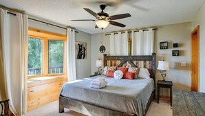 Quarto com cama de madeira, ventoinha no teto, janela com cortinas e mesa de cabeceira com abajur.