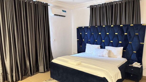 Een slaapkamer met een bed, nachtkastje, telefoon en een wandairconditioner.
