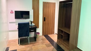 Een kamer met een bureau, stoel, televisie, kledingkast en een deur.