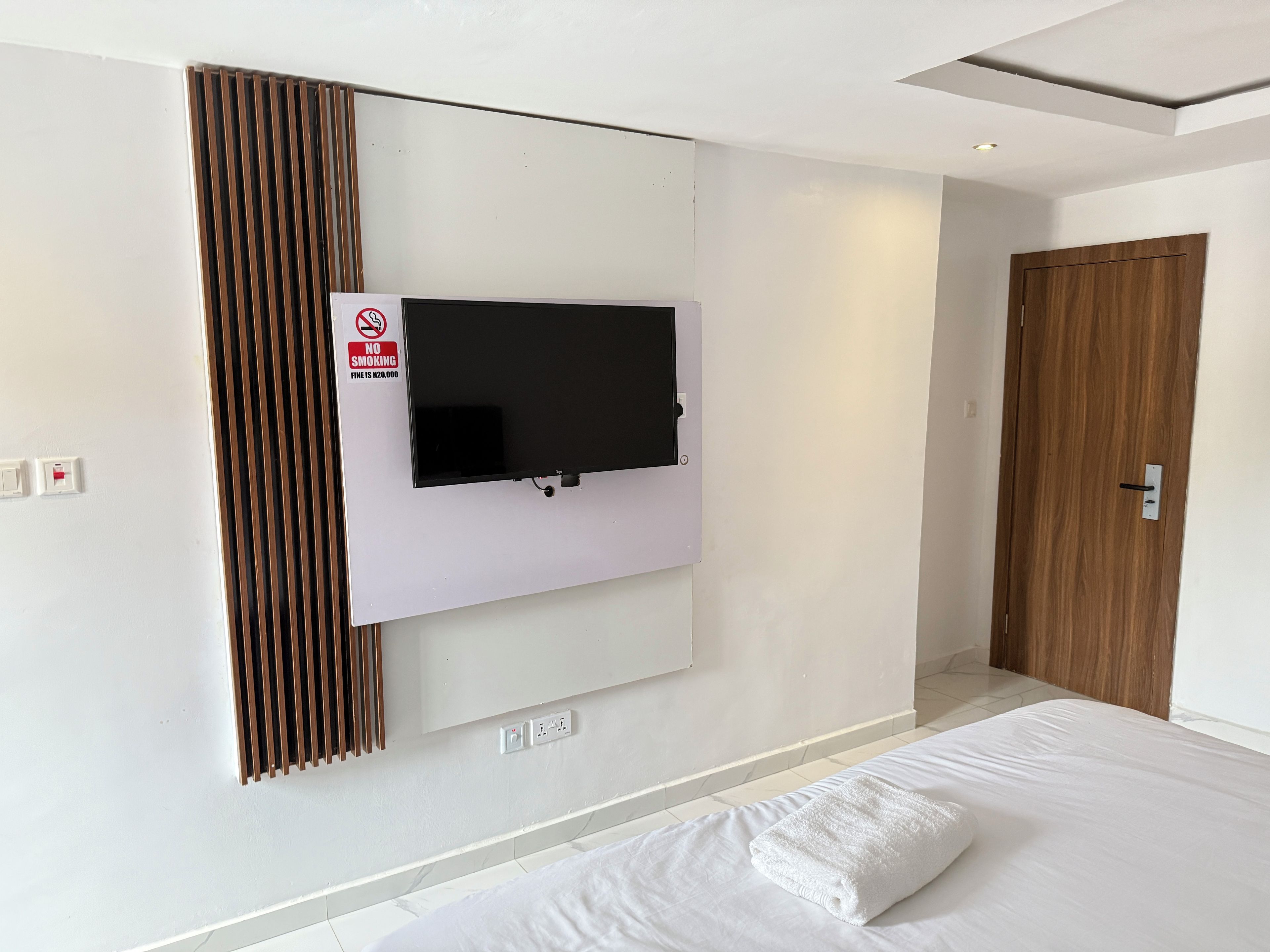 Una habitación de hotel moderna con un televisor montado, una puerta de madera y una cama bien hecha.