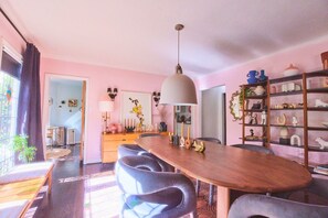 A dining area with a wooden table, grey upholstered chairs, a pendant light, and a bookshelf with decorative items. - Peaceful 3-bedroom house in West Hollywood (West Hollywood)