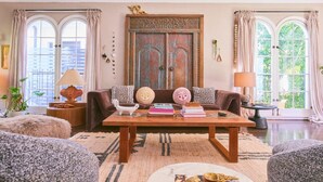 Ein gemütliches Wohnzimmer mit einer braunen Couch, einem Holztisch und einem großen Fenster mit Vorhängen.