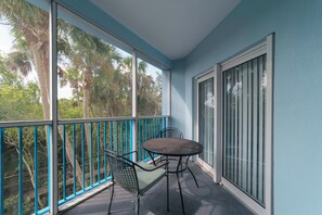 Un balcone con tavolo e sedie, ampie finestre e vista su palme.