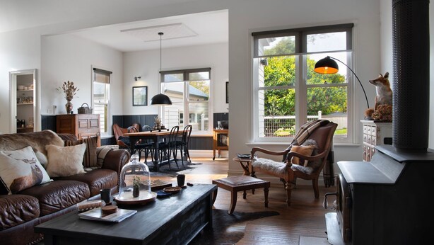 Ein geräumiges Wohnzimmer mit einer Ledersofa, einem Holztisch und einem Kamin. Es gibt einen Essbereich mit Tisch und Stühlen, sowie große Fenster mit Blick ins Freie.