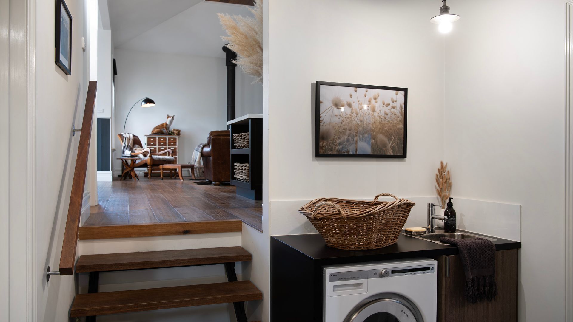 A laundry area with a washing machine, a wicker basket, and a framed picture on the wall.