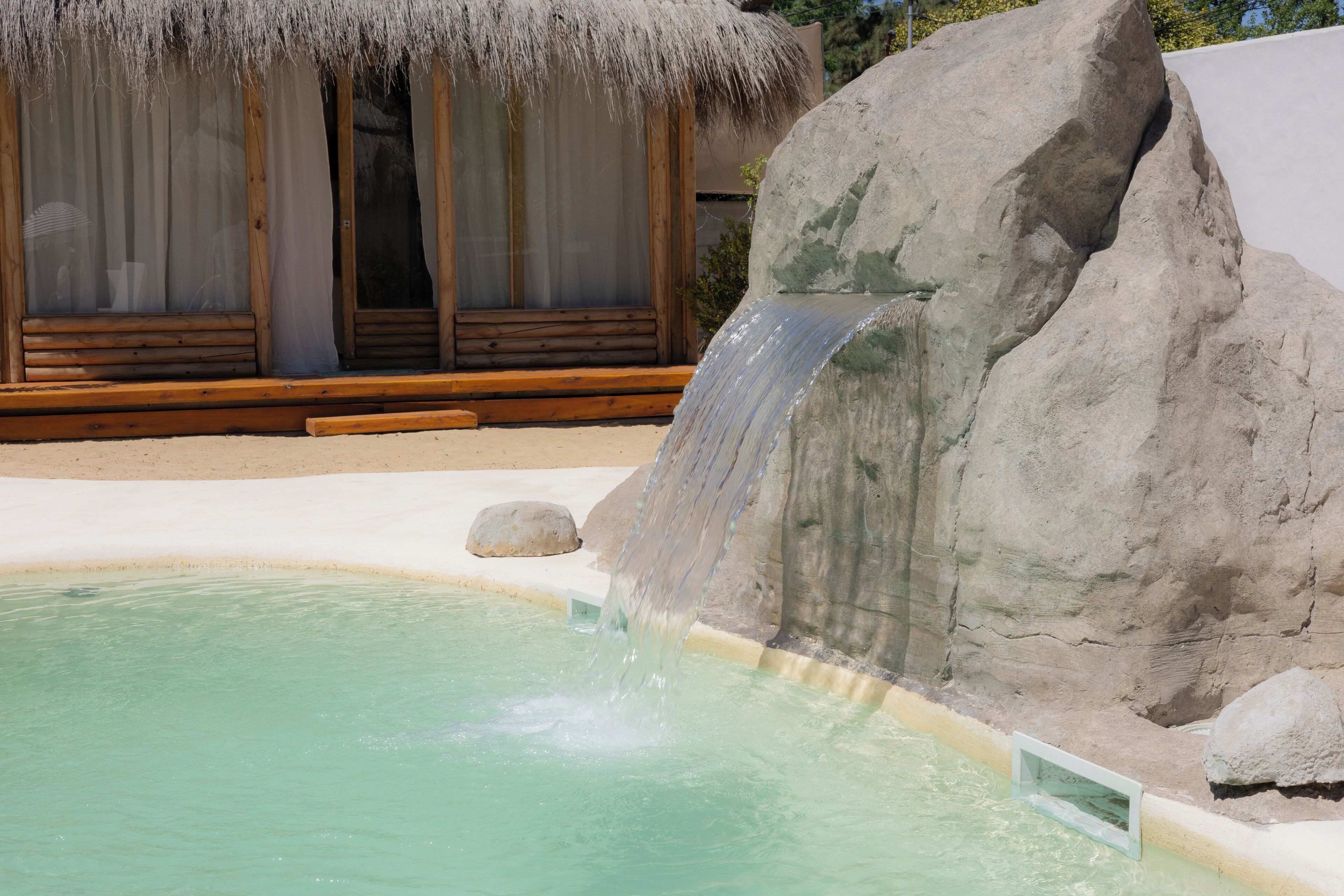A pool with a waterfall feature, a thatched-roof structure, and a large rock formation.