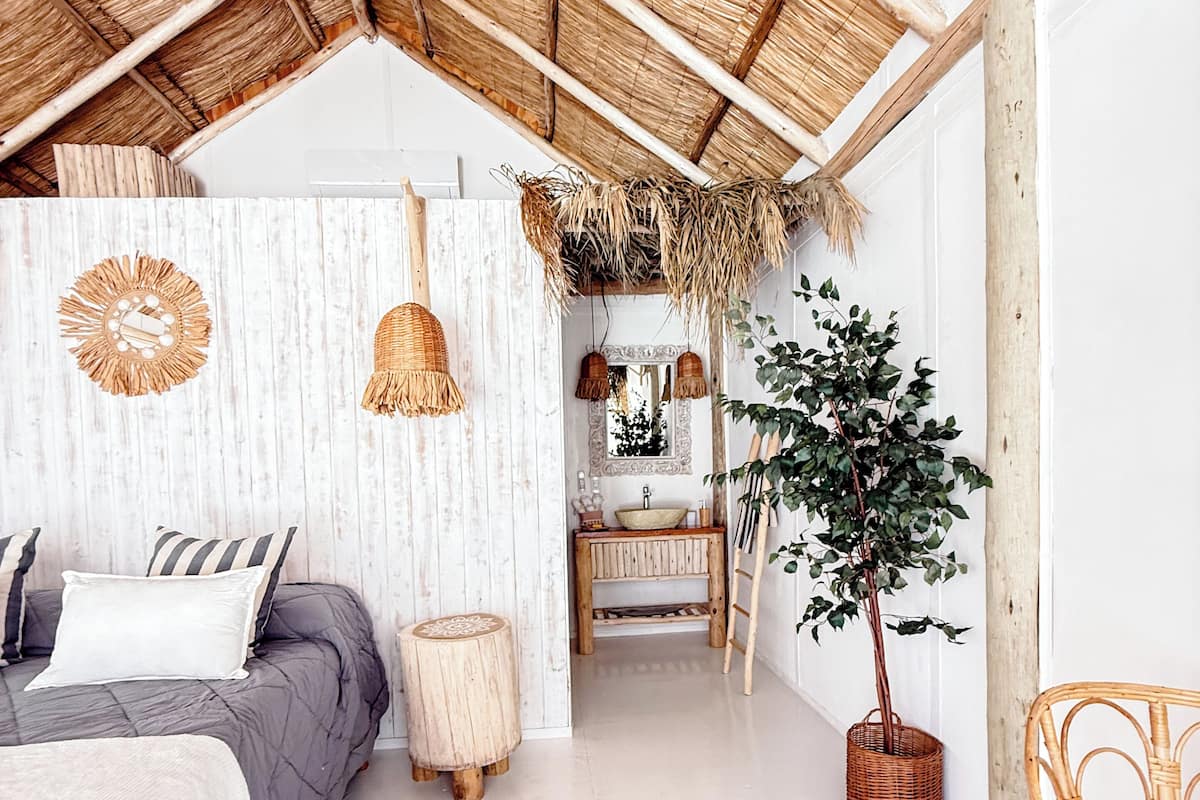 A bedroom with a bed, bedside tables, a mirror, a potted plant, and a wicker chair.