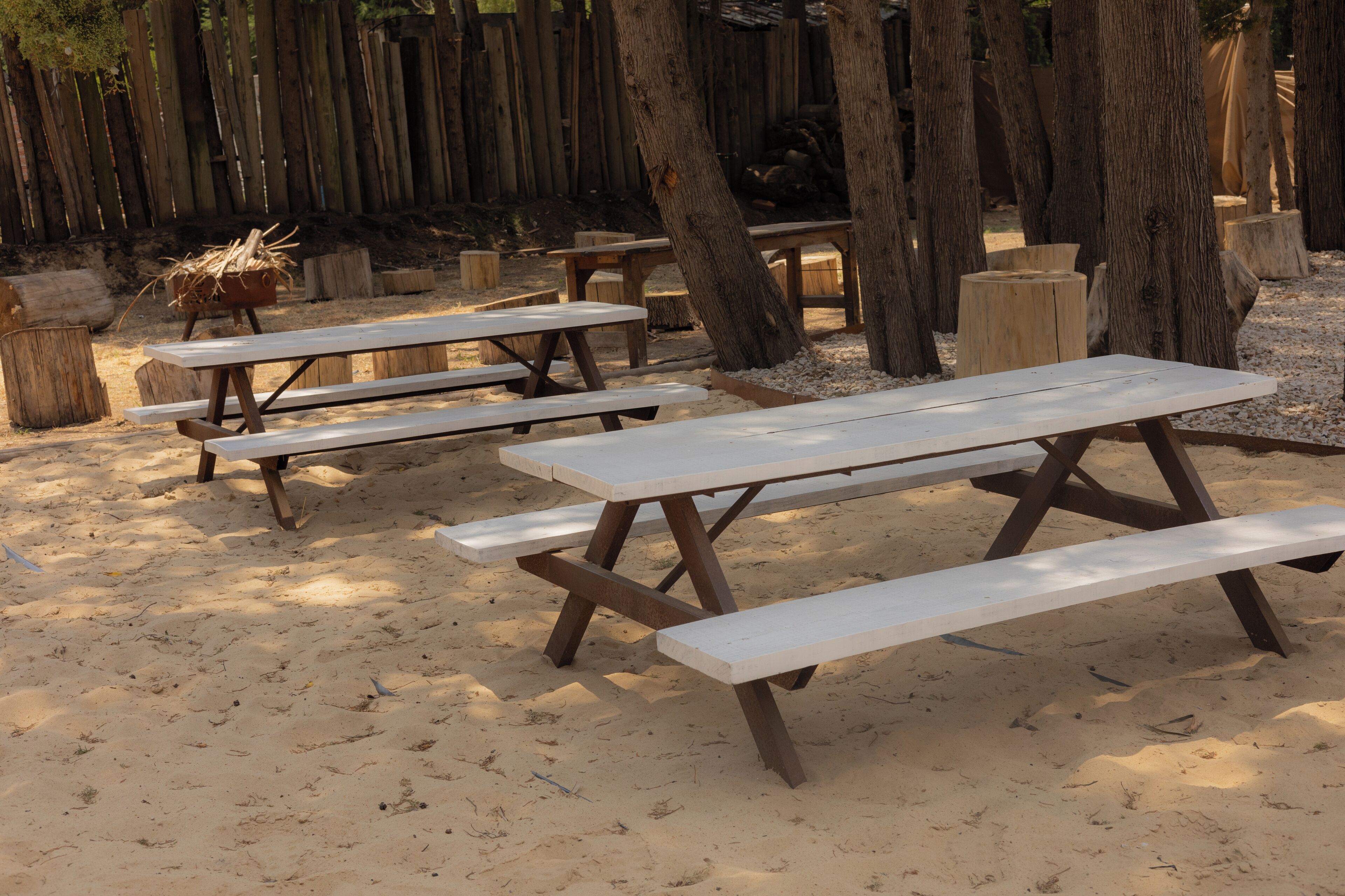 A sandy outdoor area with picnic tables and wooden benches.