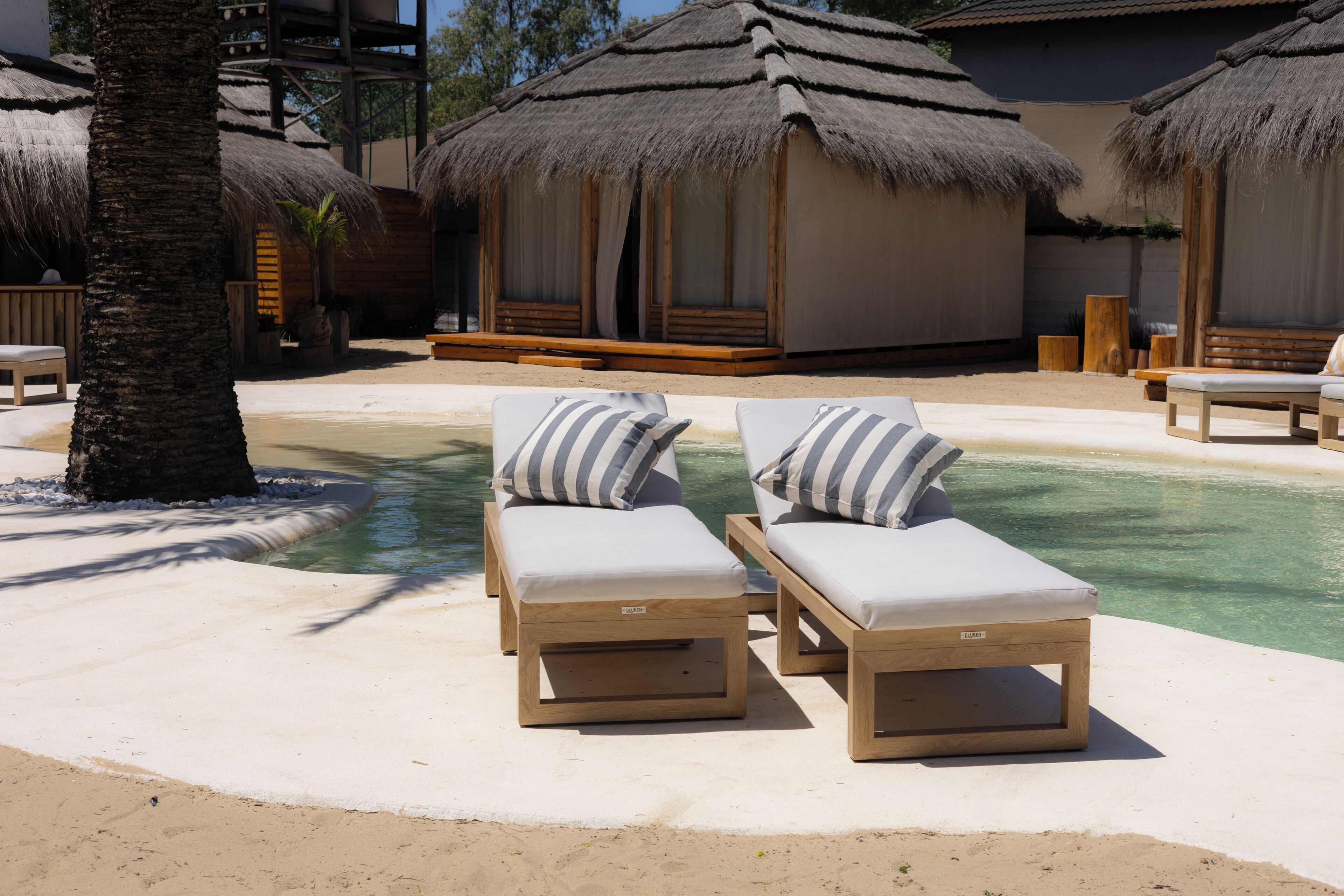 Un área junto a la piscina con sillones de descanso y estructuras de techo de paja.