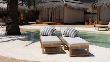 Un área junto a la piscina con sillones de descanso y estructuras de techo de paja.