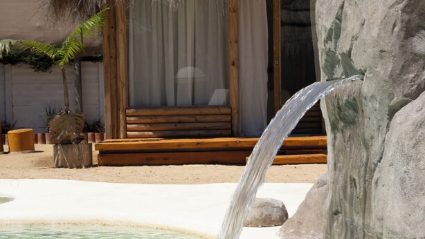 A pool with a waterfall feature, a wooden bench, and a thatched-roof structure. - Tribu Eco Beach (Francisco Alvarez)