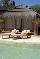 Un espacio de descanso frente a la playa con dos sillones de madera y una estructura de techo de paja.