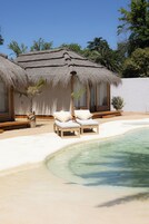 Un resort frente al mar con cabañas de techo de paja, piscina y sillones de descanso.