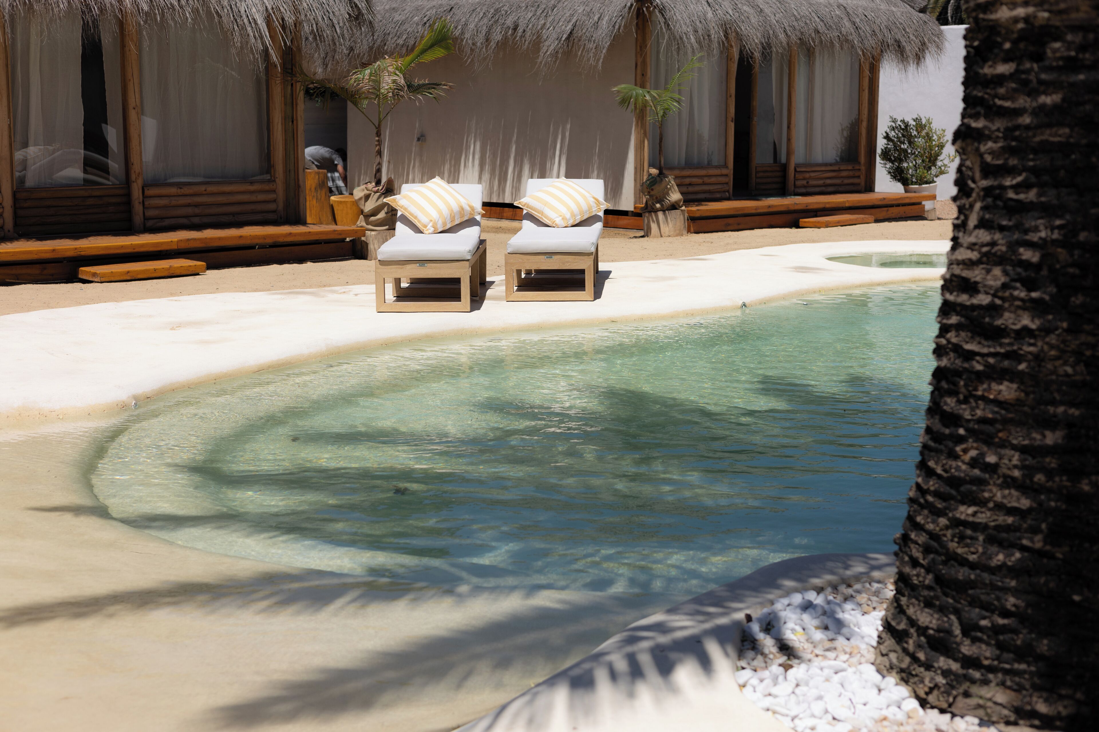 A pool area with two lounge chairs and a thatched-roof structure.