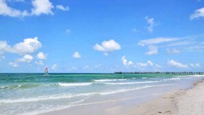 Ein Strand mit blauem Himmel, sanften Wellen und einem fernen Steg.